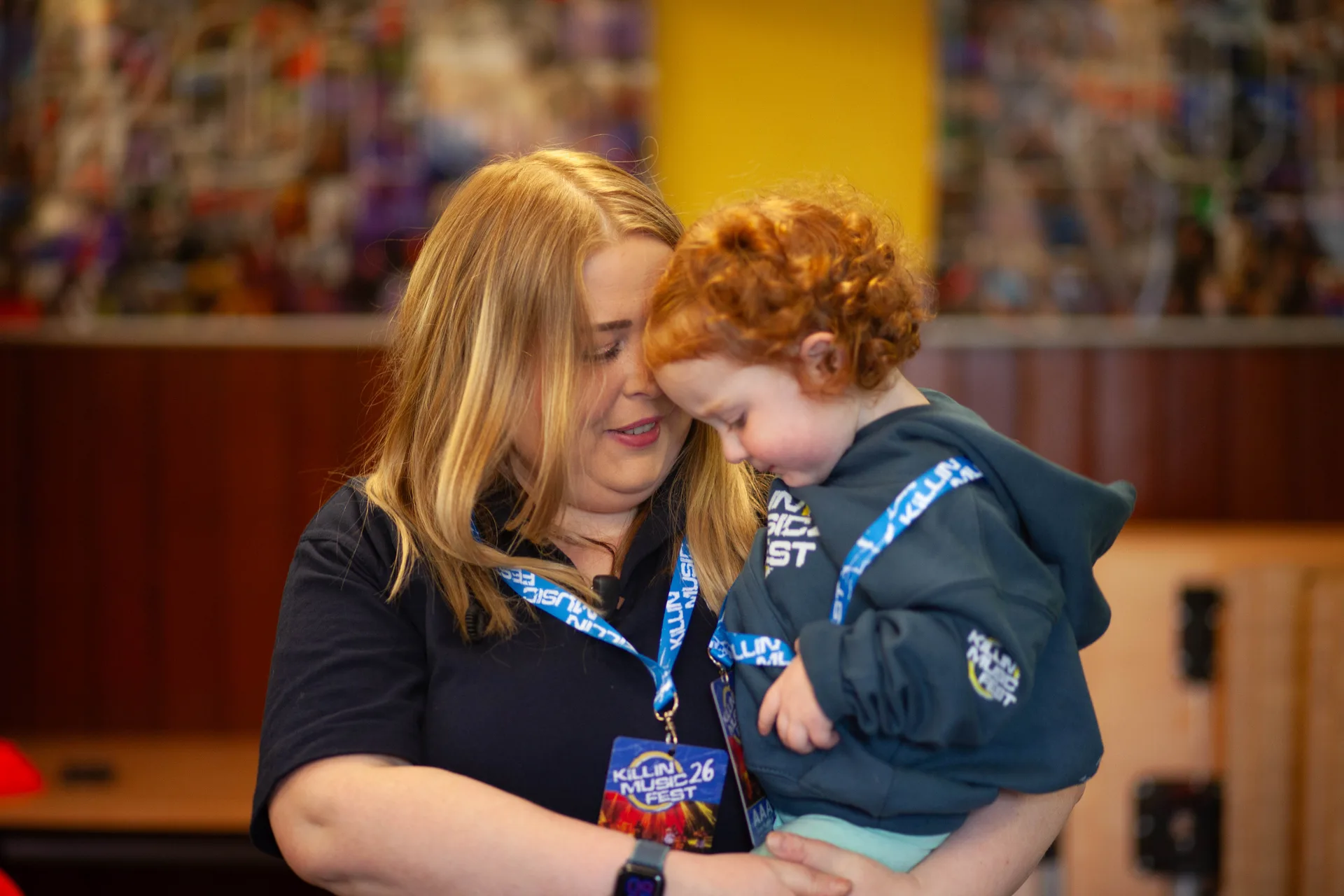 A volunteer resting her head against a young child in a festival hoodie