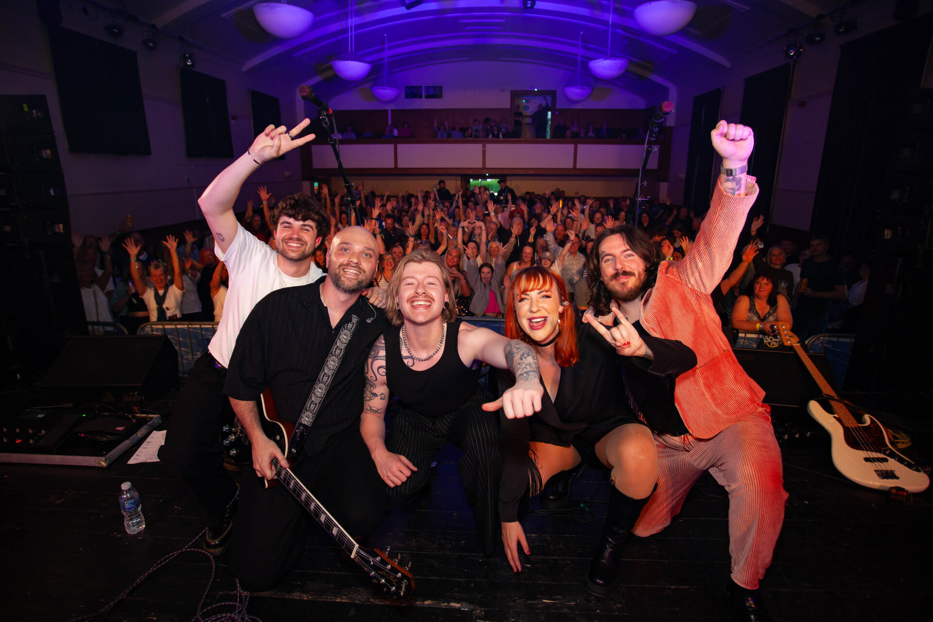 The full band crouched at the stage edge in front of a packed McLaren Hall