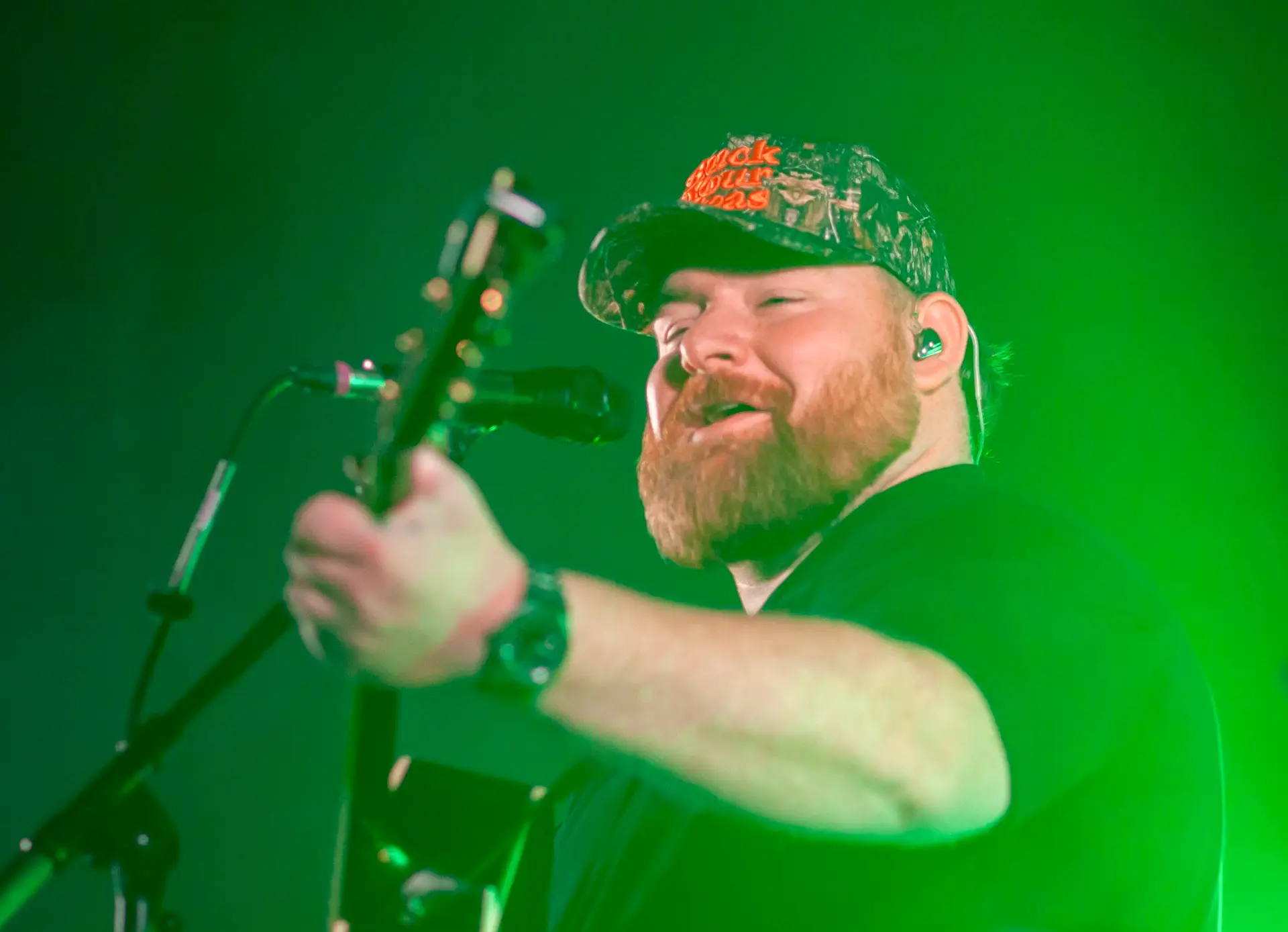 Bearded singer performing under green stage lights