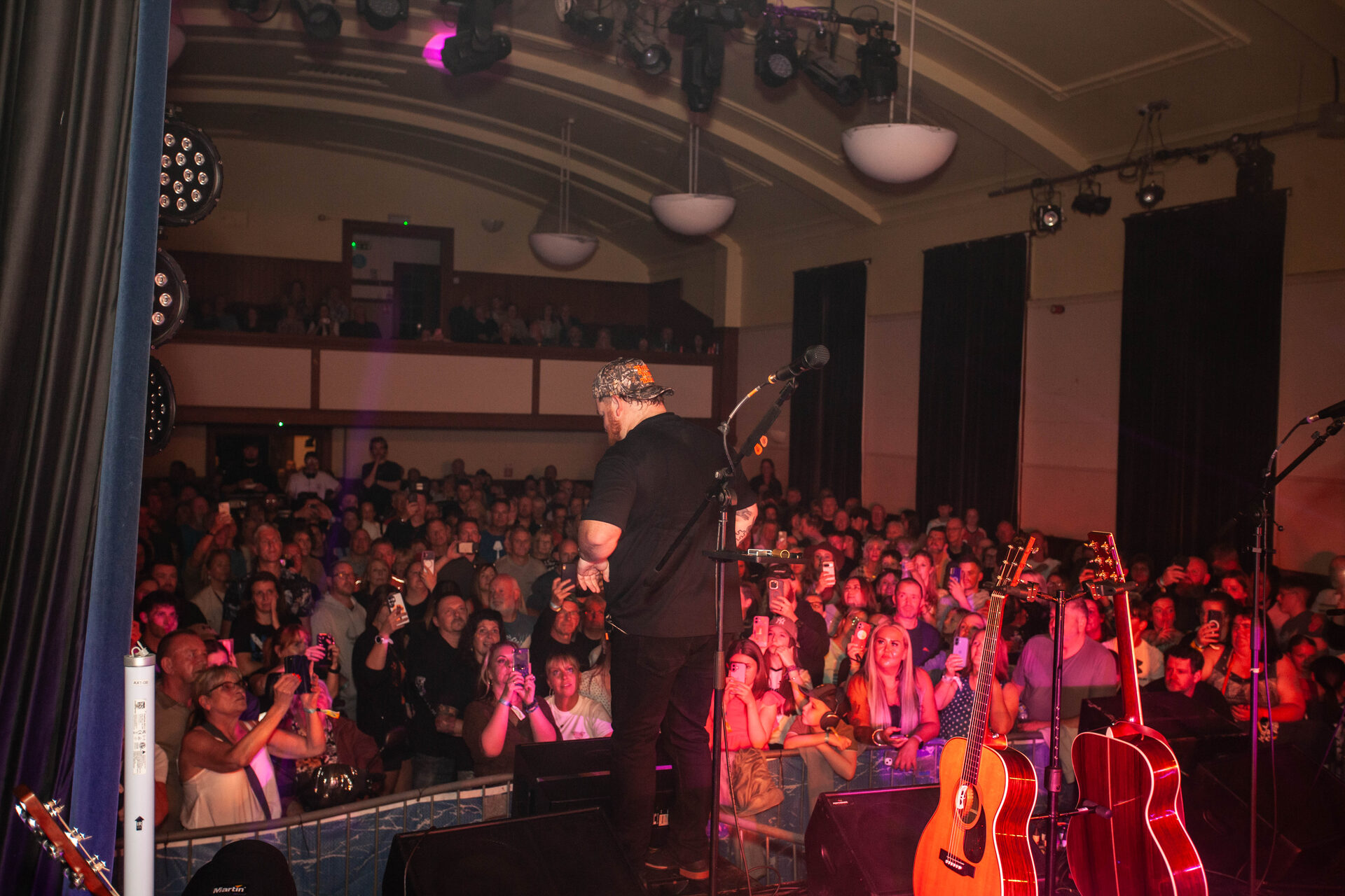 A packed McLaren Hall and balcony seen from the stage, phones held aloft