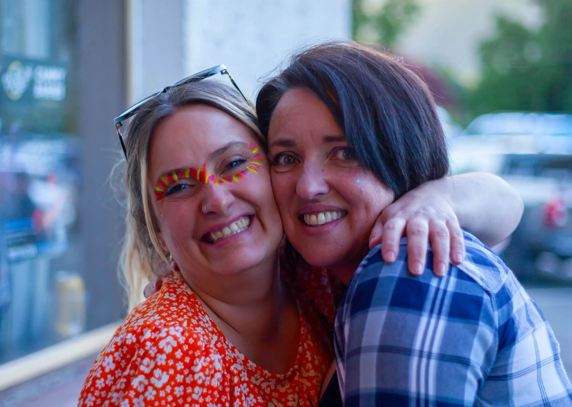 Two friends cheek to cheek with neon festival face paint