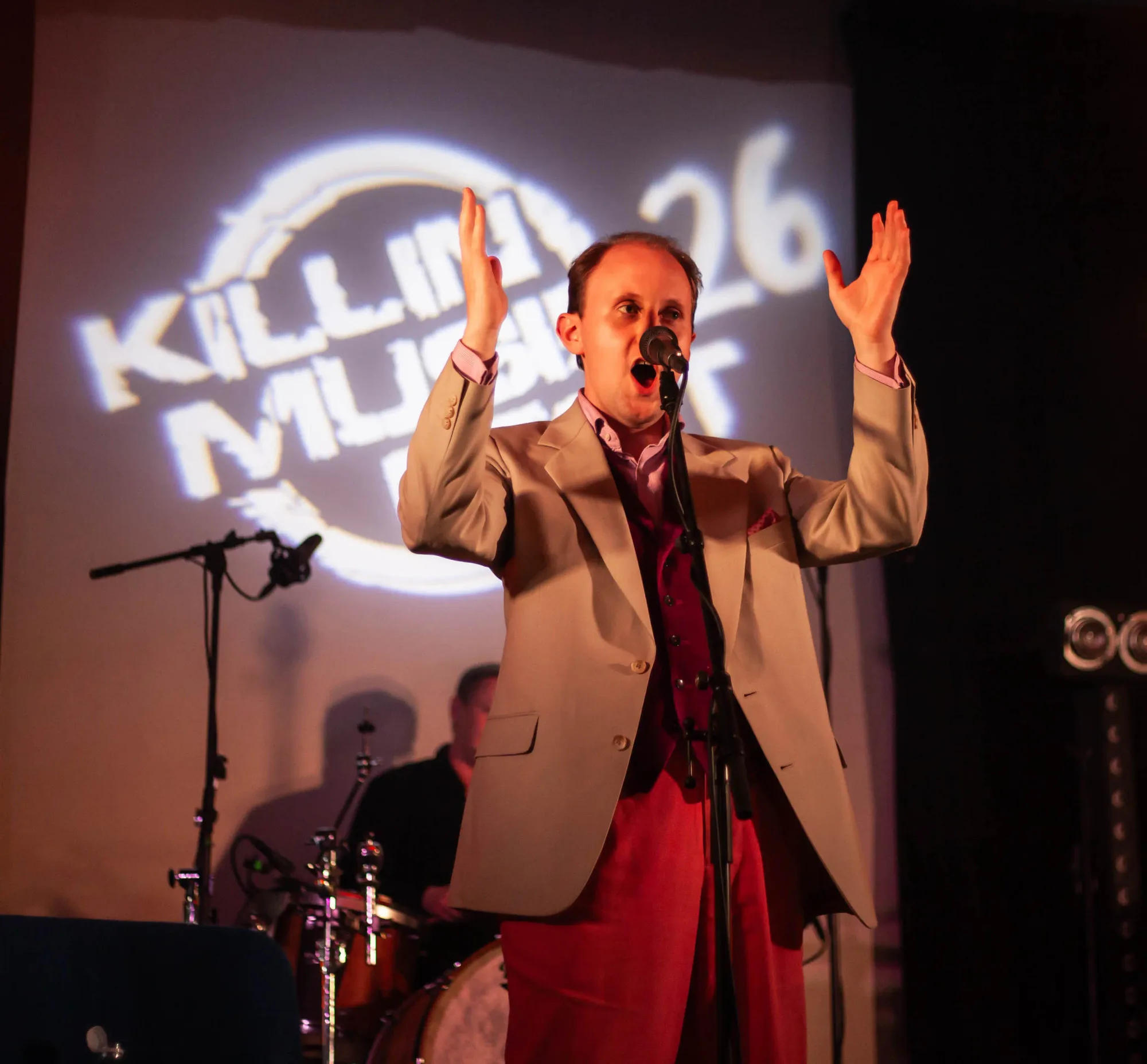 Ruairidh Gray singing with his hands raised in front of the projected festival logo