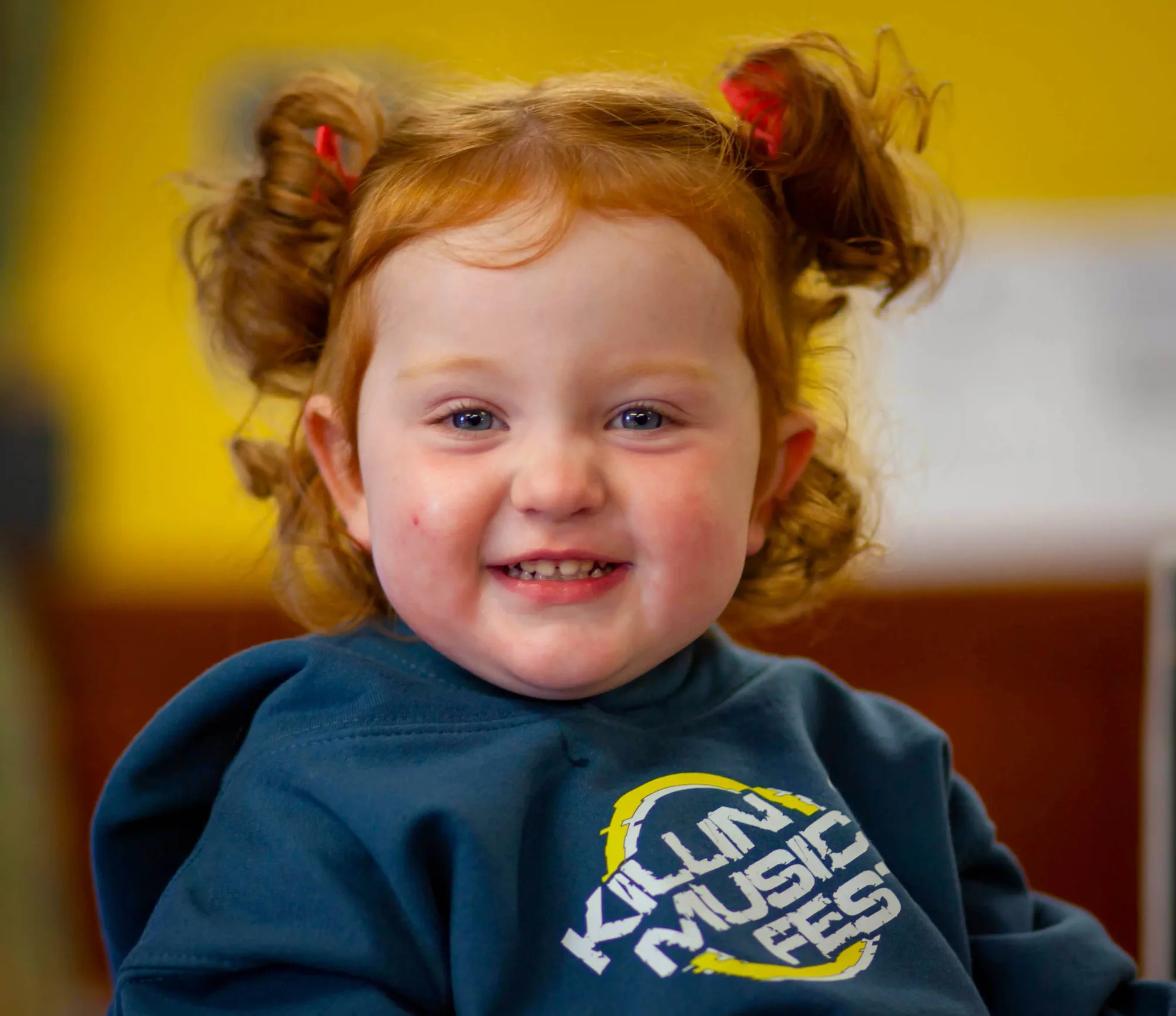 A young child in pigtails and a festival hoodie grinning to camera